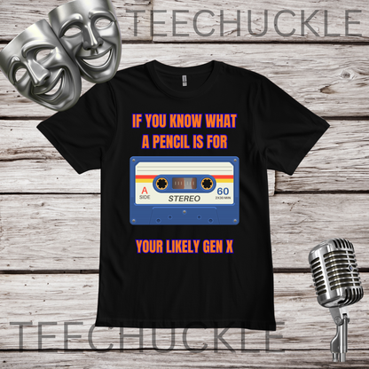 A black short-sleeve graphic t-shirt displayed flat on a rustic wood background, featuring a cassette tape graphic with the text "IF YOU KNOW WHAT A PENCIL IS FOR YOU'RE LIKELY GEN X". The image includes decorative props like two silver theater masks, a vintage microphone,.