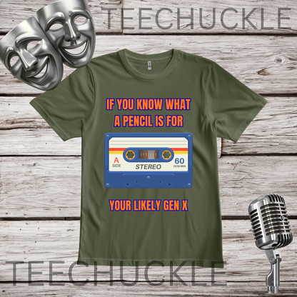 A green graphic t-shirt displayed on a rustic wood background, featuring a retro cassette tape design with the text 'IF YOU KNOW WHAT A PENCIL IS FOR YOUR LIKELY GEN X'. The image includes decorative props like two silver comedy masks and a vintage microphone