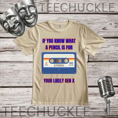 A sand graphic t-shirt displayed on a rustic wood background, featuring a retro cassette tape design with the text 'IF YOU KNOW WHAT A PENCIL IS FOR YOUR LIKELY GEN X'. The image includes decorative props like silver comedy and tragedy masks, a vintage microphone.