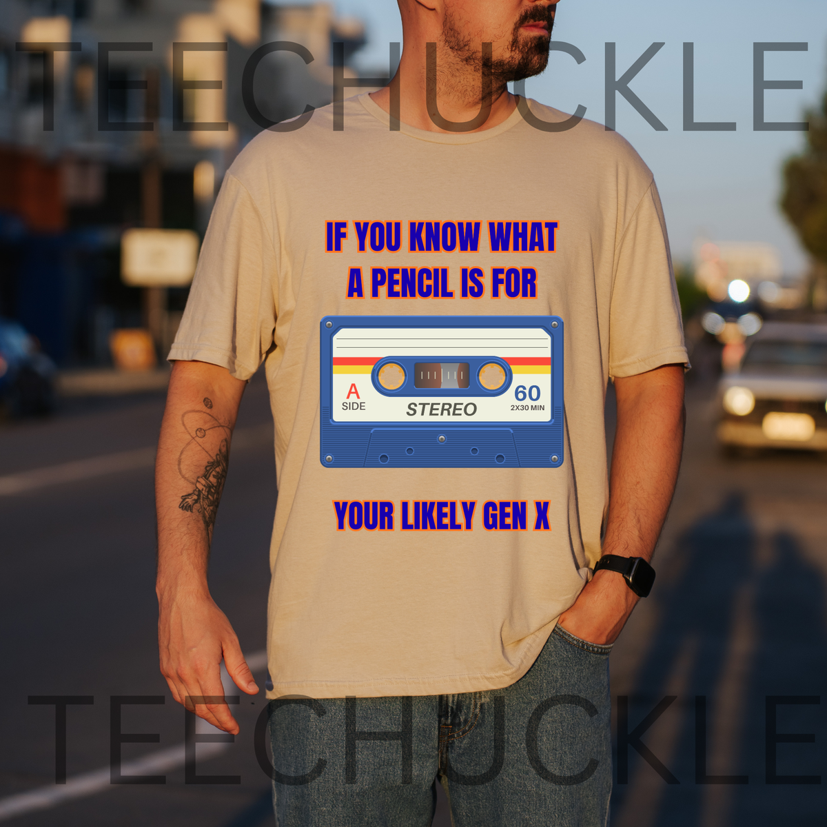 A man wearing a sand graphic t-shirt with a retro cassette tape design and the text 'IF YOU KNOW WHAT A PENCIL IS FOR YOUR LIKELY GEN X' in blue and purple. The background is a blurred street at sunset.