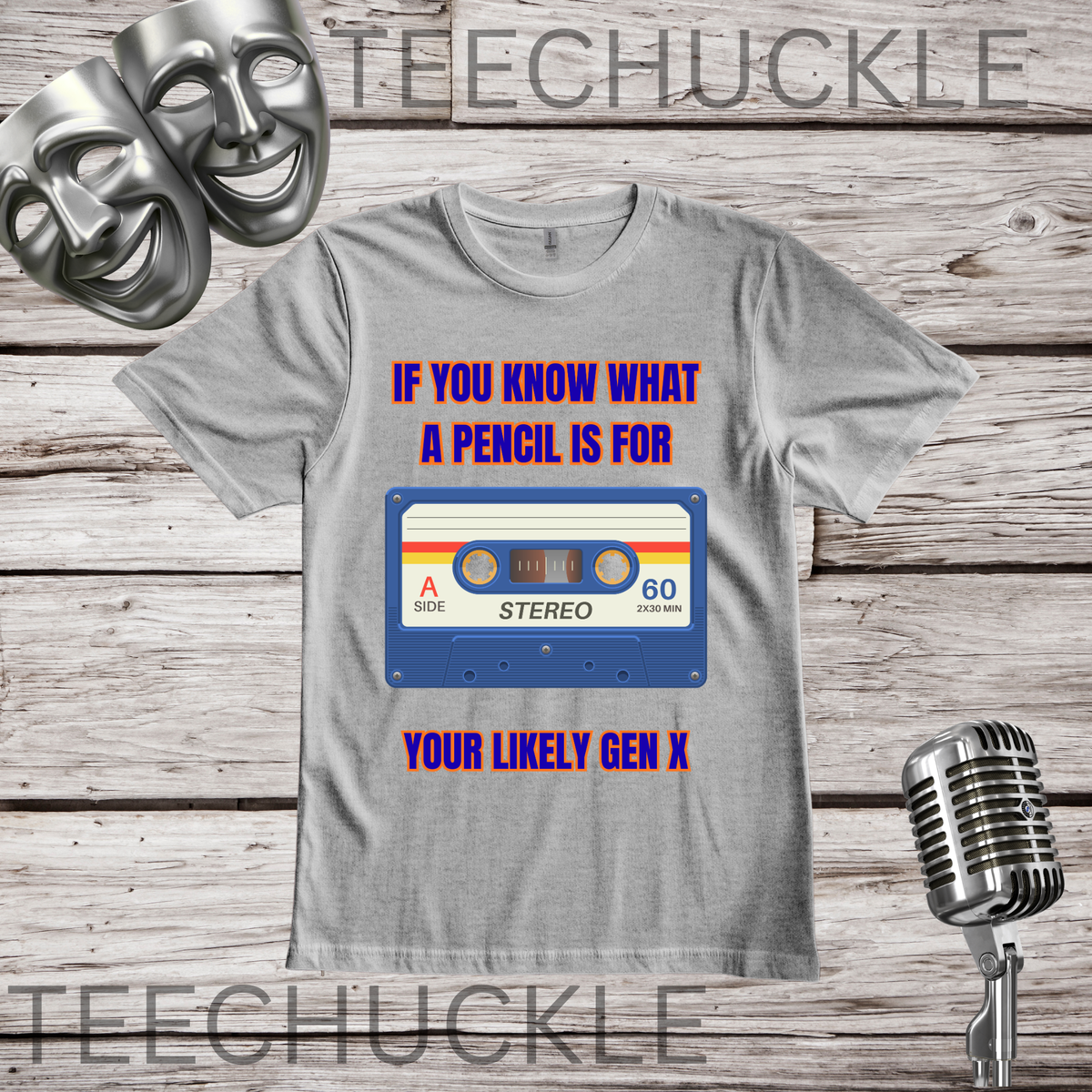 A gray graphic t-shirt displayed on a rustic wood background, featuring a retro cassette tape design with the text 'IF YOU KNOW WHAT A PENCIL IS FOR YOUR LIKELY GEN X'. The t-shirt is styled with silver comedy masks and a vintage microphone