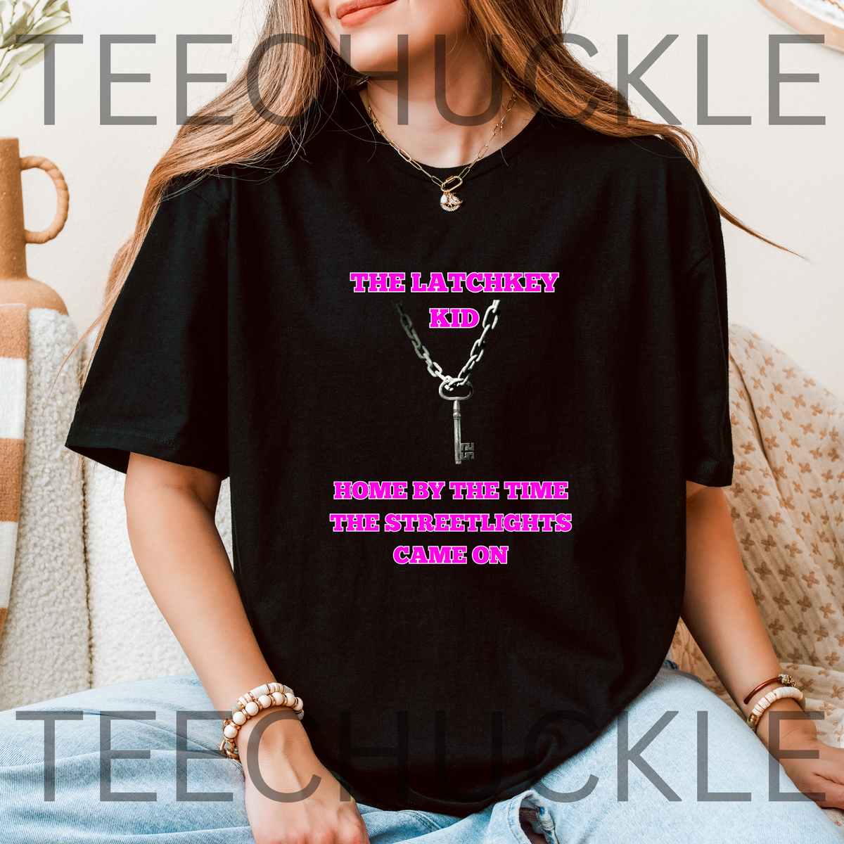 A woman wearing a black graphic t-shirt with pink text that reads 'THE LATCHKEY KID HOME BY THE TIME THE STREETLIGHTS GONE ON' and a silver key-and-chain illustration. 