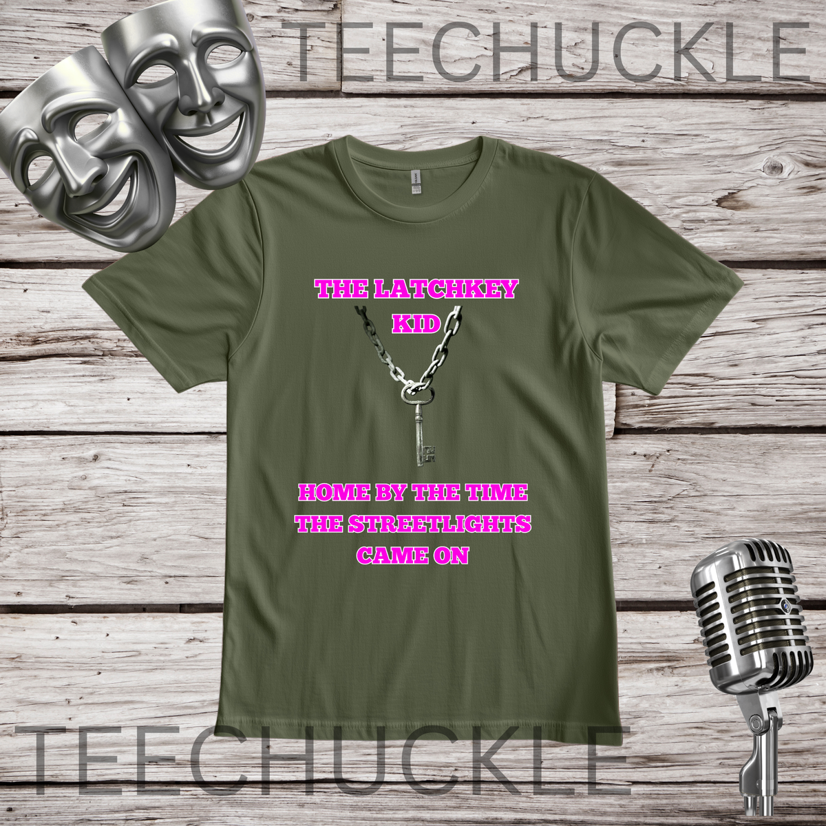 A green graphic t-shirt displayed on a rustic wood background, featuring a key and chain with the pink text 'THE LATCHKEY KID HOME BY THE TIME THE STREETLIGHTS CAME ON'. The image includes decorative props like silver theater masks and a vintage microphone