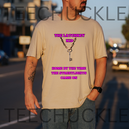 A man wearing a sand graphic t-shirt with a pink text that reads 'THE LATCHKEY KID' and 'HOME BY THE TIME THE STREETLIGHTS CAME ON' with a ley and chain design