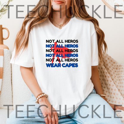 A woman wearing a white graphic T-shirt with the text 'NOT ALL HEROS' repeated in black and blue, with a red superhero behind it, and "wear capes" below, seated indoors.