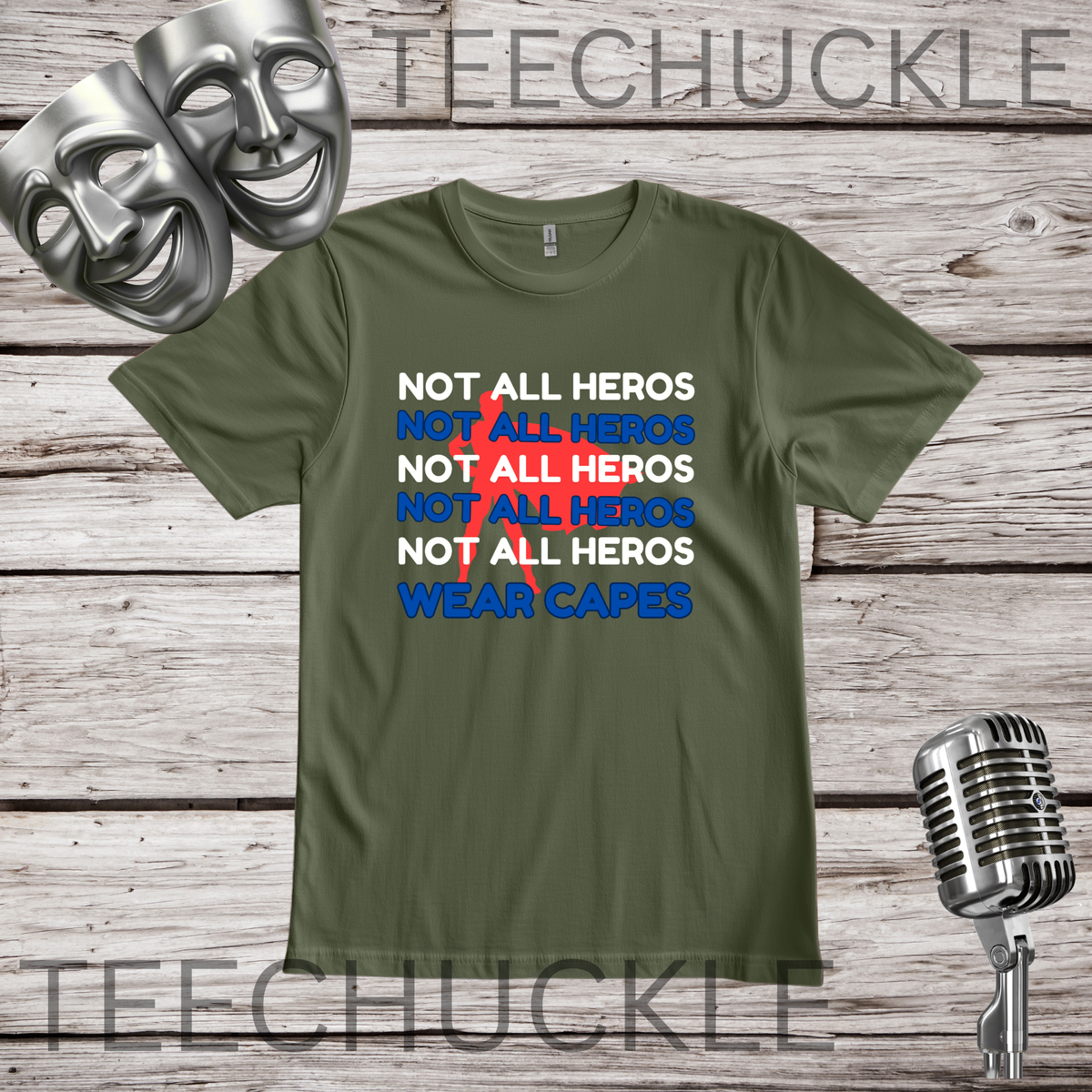 A green graphic t-shirt displayed on a rustic wooden background, featuring a text design that reads 'NOT ALL HEROS' in white and blue, with a red superhero behind it, and finished with 'WEAR CAPES' in blue. The t-shirt is framed by silver comedy masks on the top left, a vintage microphone on the bottom right.