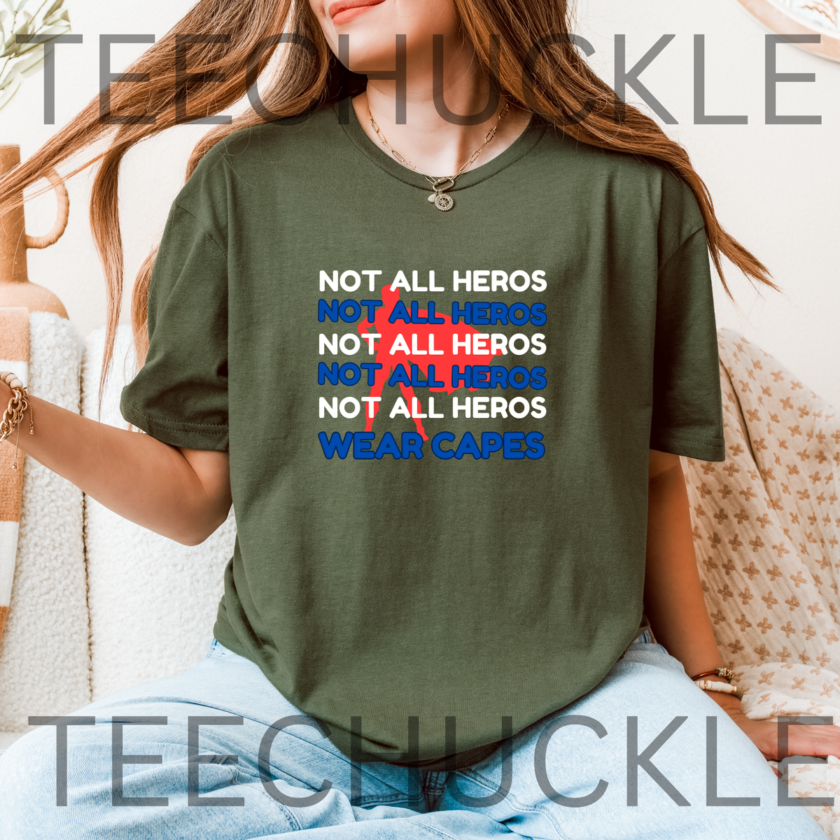 A woman wearing a green graphic t-shirt with the slogan 'NOT ALL HEROS WEAR CAPES' printed in white, blue, and red superhero graphic behind it. 