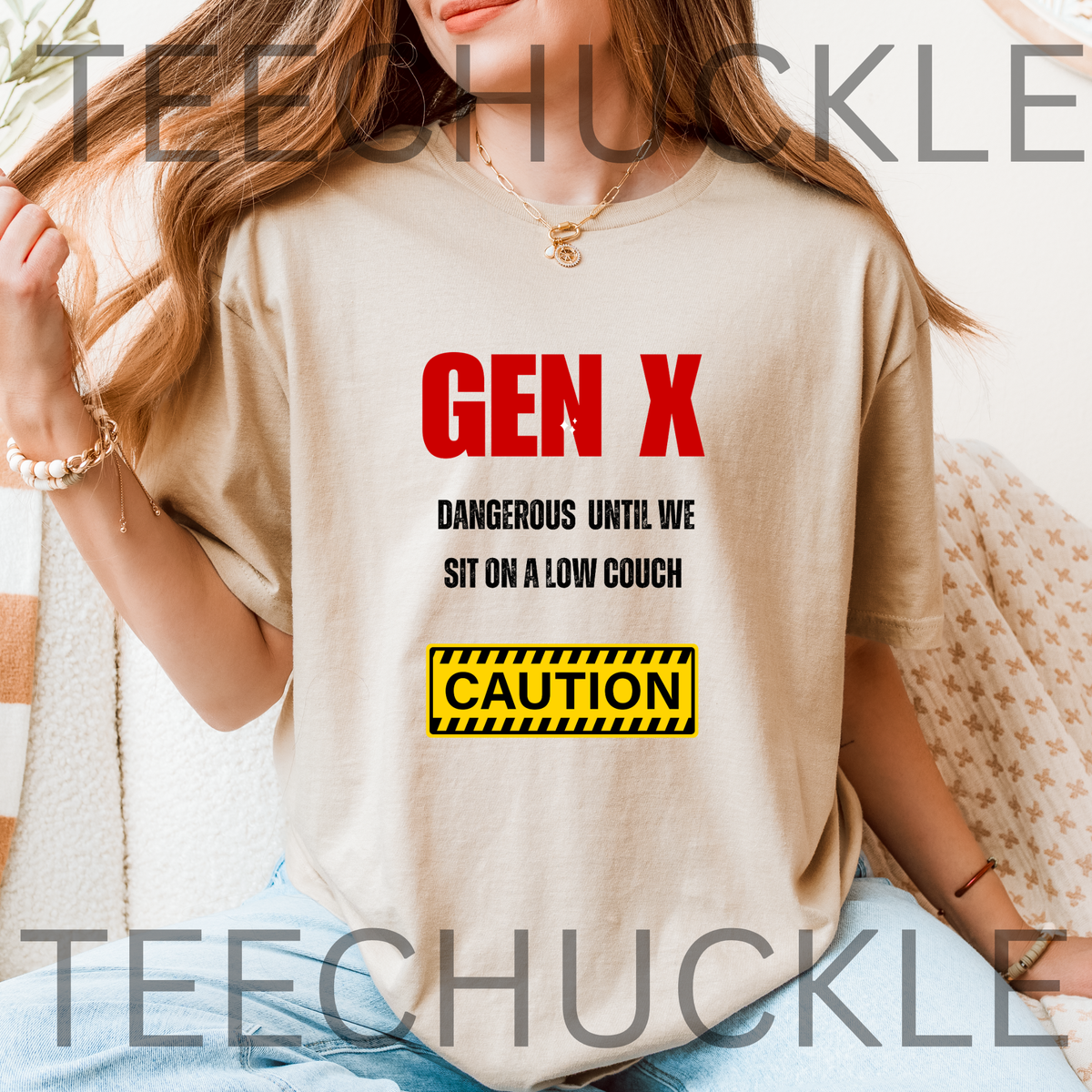 A woman wearing a sand graphic t-shirt with a red and black 'GEN X DANGEROUS UNTIL WE SIT ON A LOW COUCH' slogan and a yellow caution box graphic.
