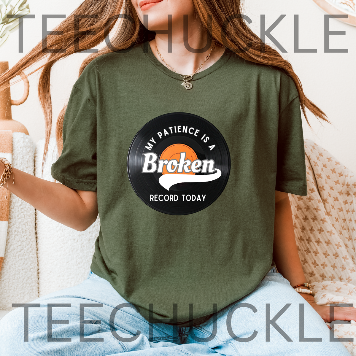 A woman wearing a green t-shirt with a vinyl record graphic that reads 'MY PATIENCE IS A BROKEN RECORD TODAY'.  The model is seated on a patterned beige sofa.