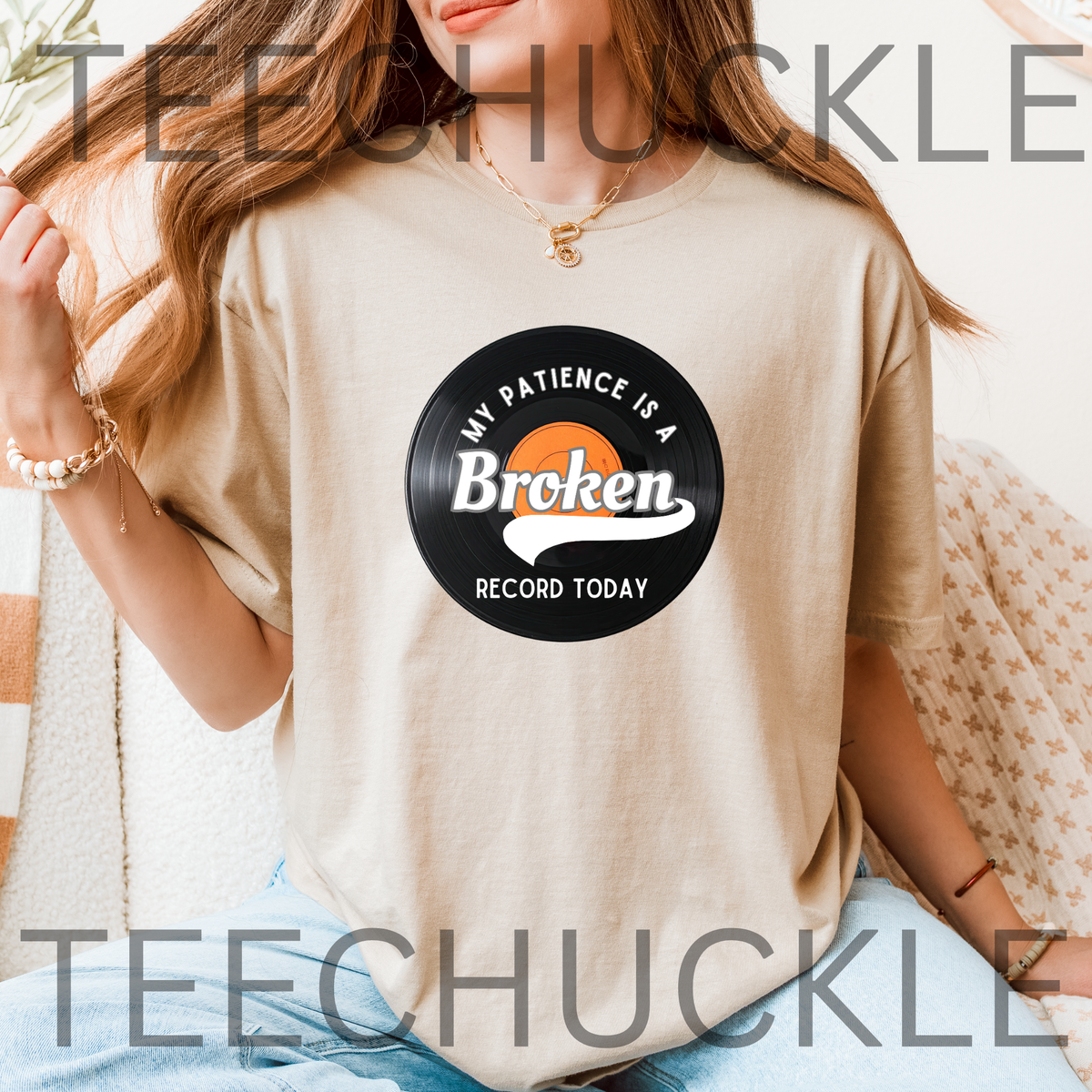 A woman wearing a sand t-shirt with a vinyl record graphic that reads 'MY PATIENCE IS A BROKEN RECORD TODAY'. 