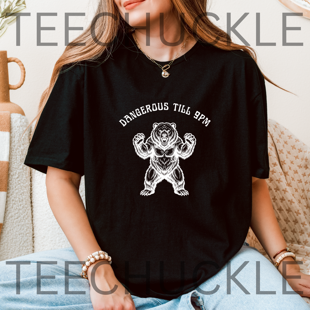 A woman wearing a black graphic t-shirt with a white bear illustration and the text 'DANGEROUS TILL 9PM'.