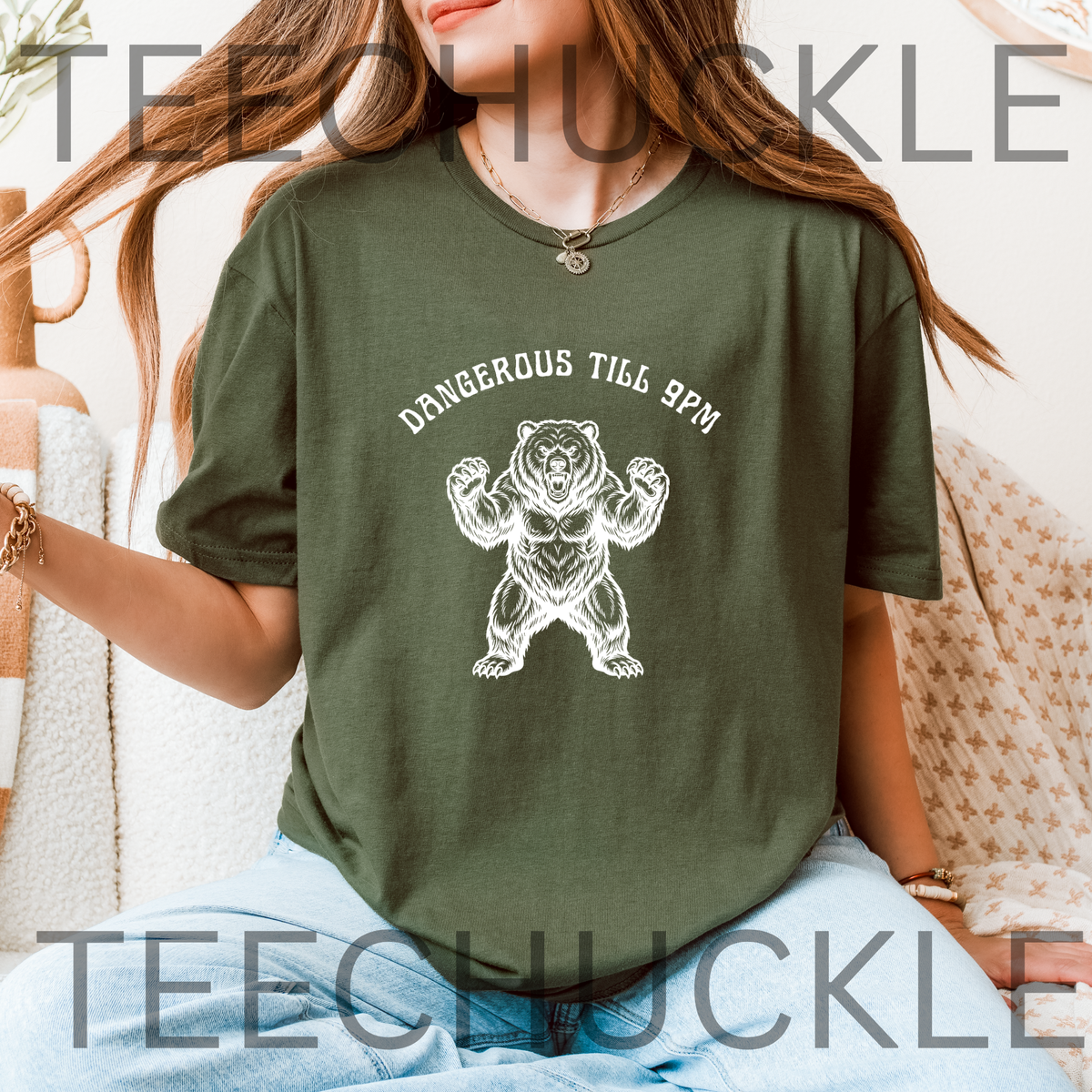 A woman wearing an green graphic t-shirt with a white bear illustration and the text 'DANGEROUS TILL 9PM'.