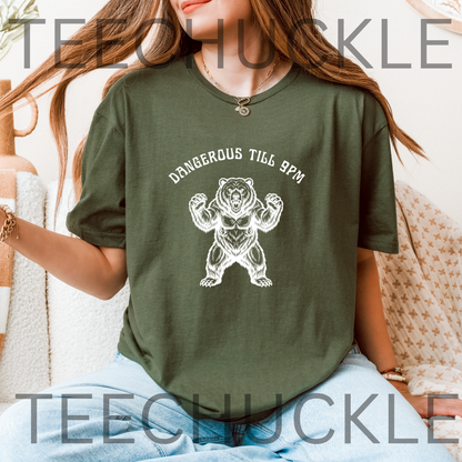 A woman wearing an green graphic t-shirt with a white bear illustration and the text 'DANGEROUS TILL 9PM'.