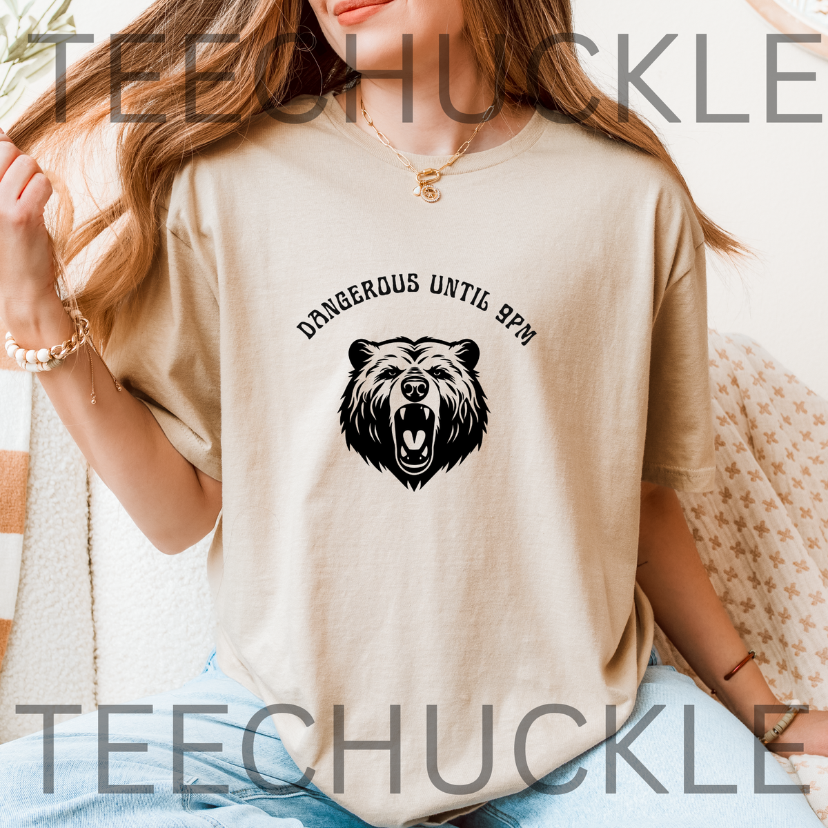 A woman wearing a sand graphic t-shirt with a black bear head design and the text 'DANGEROUS UNTIL 8PM' on the chest.