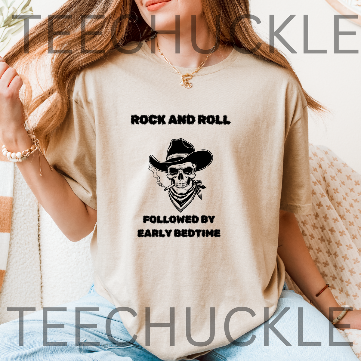 A woman wearing a sand graphic t-shirt with a black skull cowboy print and the text 'ROCK AND ROLL FOLLOWED BY EARLY BEDTIME'.