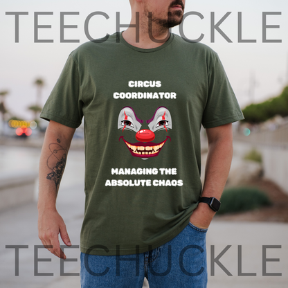 A man wearing an green graphic t-shirt with a creepy clown face and white text that reads 'circus cordinator, managing the absolute chaos' The background is a blurred outdoor street scene