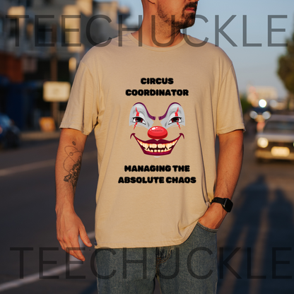 A man wearing a sand graphic t-shirt with a clown face and the text 'CIRCUS COORDINATOR MANAGING THE ABSOLUTE CHAOS' on the front, standing outdoors on a street at sunset.
