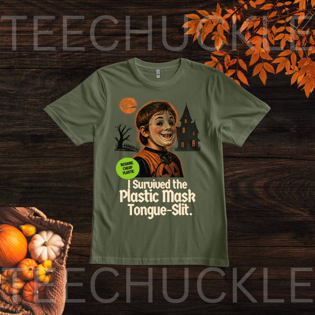 A green graphic t-shirt displayed flat on a dark wood background with autumn-themed props like pumpkins and orange leaves. The graphic features a cartoon of a smiling child with a plastic mask and a tongue slit, with the text 'I Survived the Plastic Mask Tongue-Slit.
