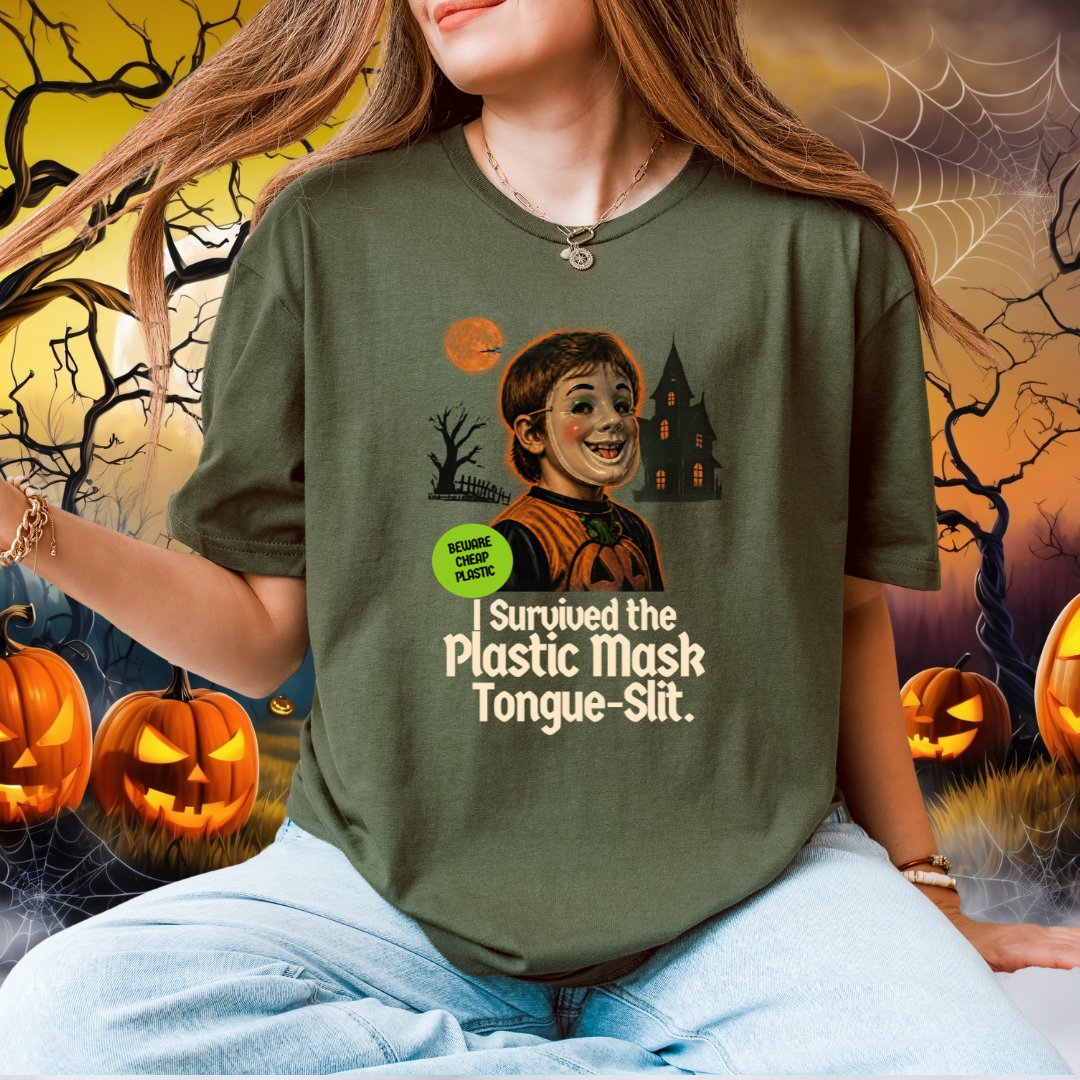 A woman wearing a green graphic t-shirt with a Halloween-themed print that reads 'I Survived the Plastic Mask Tongue-Slit.' She is seated against a spooky Halloween background with pumpkins, cobwebs, and a haunted house.
