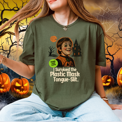 A woman wearing a green graphic t-shirt with a Halloween-themed print that reads 'I Survived the Plastic Mask Tongue-Slit.' She is seated against a spooky Halloween background with pumpkins, cobwebs, and a haunted house.