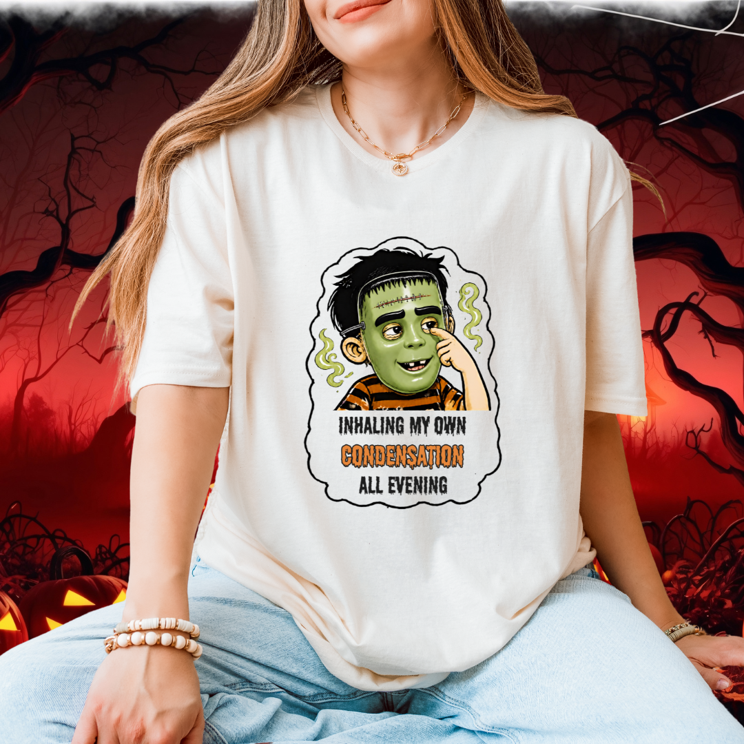 A woman wearing a cream-colored graphic t-shirt with a child in a halloween mask print and the text 'INHALING MY OWN CONDEMNATION ALL EVENING', paired with light blue jeans, set against a spooky red and black Halloween background.