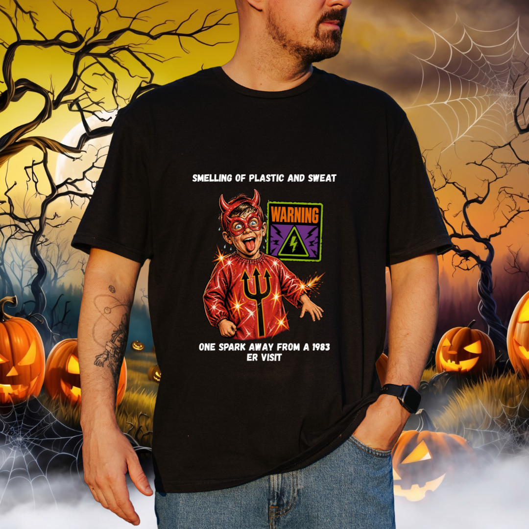 A man wearing a black graphic t-shirt with a humorous Halloween design. The design features a cartoon devil in a red suit with a trident, a 'WARNING' sign, and text reading 'SMELLING OF PLASTIC AND SWEAT' and 'ONE SPARK AWAY FROM A 1983 ER VISIT'.