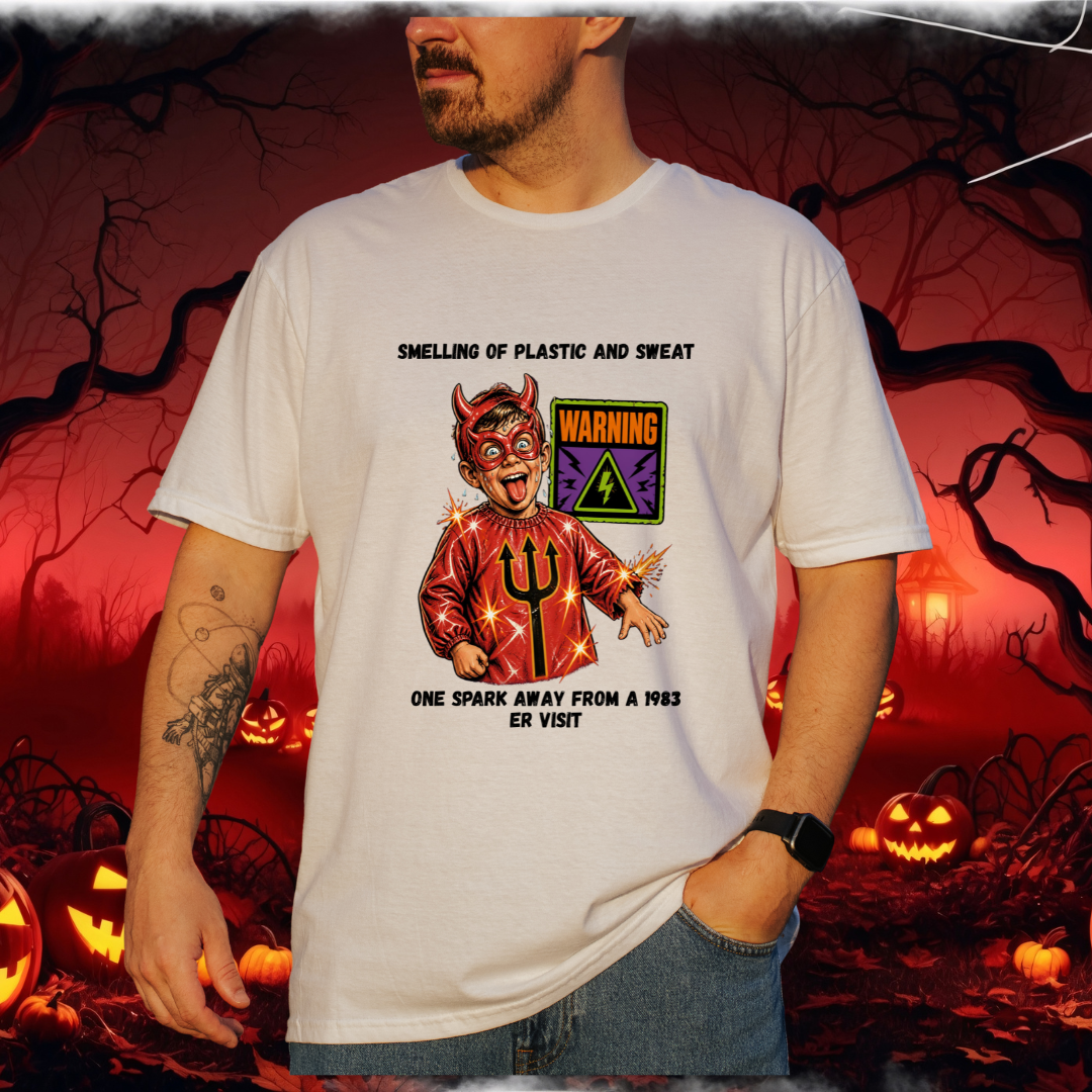 A man wearing a white graphic t-shirt with a devil illustration and text, set against a spooky Halloween background with pumpkins and bare trees.