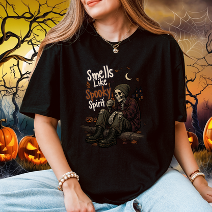 A woman wearing a black graphic t-shirt with a Halloween design that reads 'Smells Like Spooky Spirit' and features a skeleton sitting by a window. The background is a spooky, dark, and eerie Halloween-themed scene with jack-o'-lanterns, bare trees, and cobwebs.
