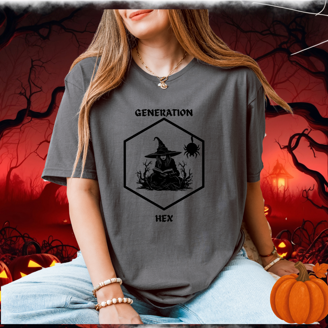 A woman wearing a dark gray graphic t-shirt with a black witch-themed design that reads 'GENERATION HEX'. The background is a spooky Halloween scene with pumpkins and bare trees.