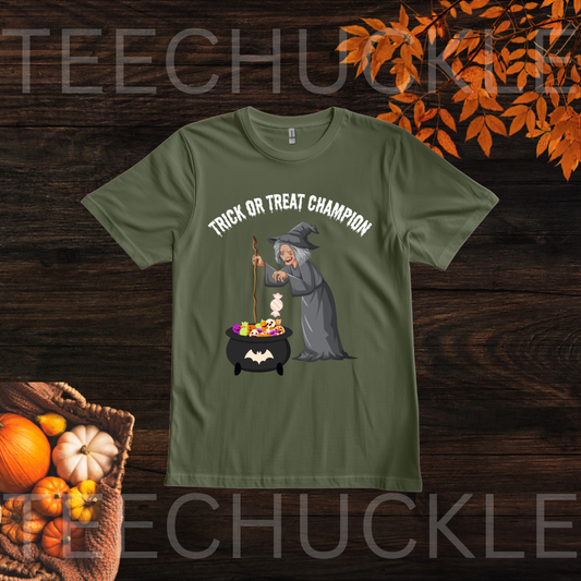 A green short-sleeve t-shirt with a 'Trick or Treat Champion' witch graphic, displayed on a dark wood background with autumn leaves and pumpkins.