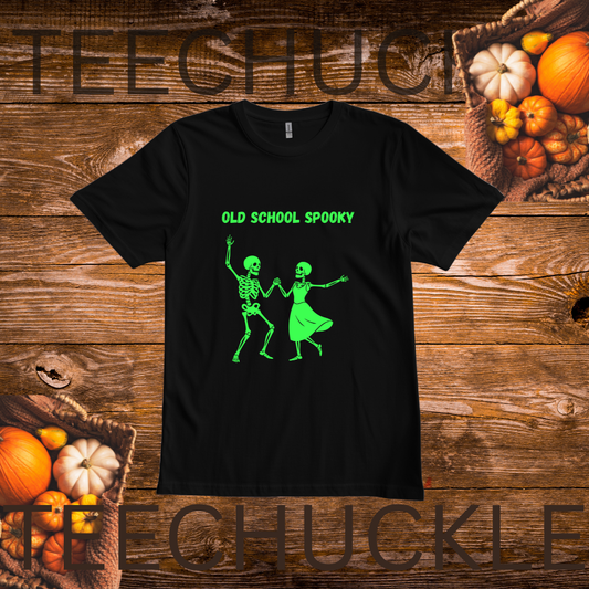 A black short-sleeve T-shirt laid flat on a rustic wooden surface with pumpkins around it. The shirt has bright green text reading 'OLD SCHOOL SPOOKY' above two green dancing skeleton figures.