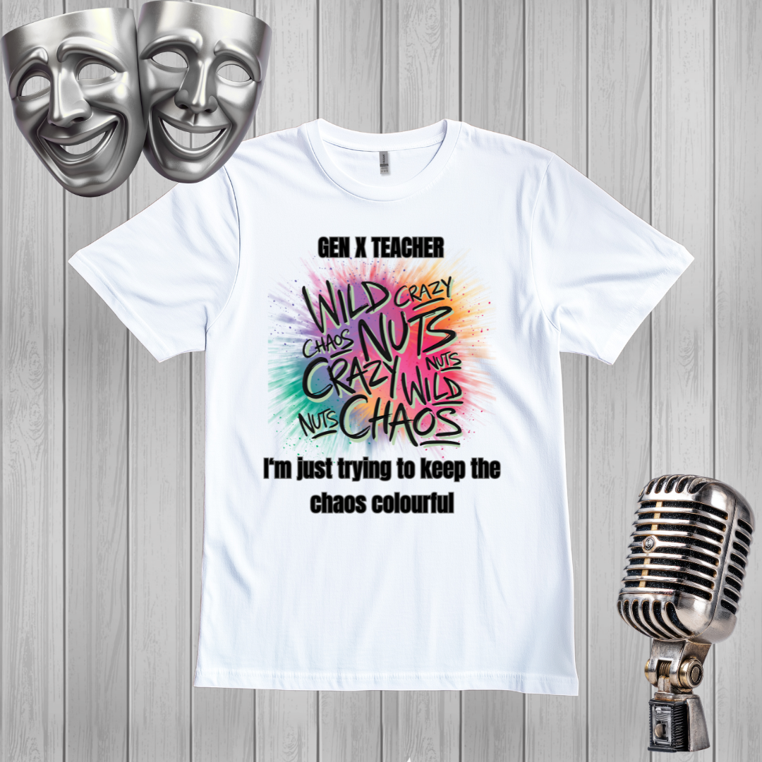 A white graphic t-shirt displayed on a gray wood plank background, flanked by silver comedy masks on the top left and a vintage-style microphone on the bottom right. The t-shirt features a colorful, hand-drawn style graphic with the words 'WILD CRAZY CHAOS NUTS' in black and multicolor lettering, with 'GEN X TEACHER' above and 'I'm just trying to keep the chaos colourful' below.