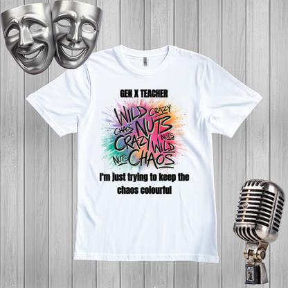 A white graphic t-shirt displayed on a gray wood plank background, flanked by silver comedy masks on the top left and a vintage-style microphone on the bottom right. The t-shirt features a colorful, hand-drawn style graphic with the words 'WILD CRAZY CHAOS NUTS' in black and multicolor lettering, with 'GEN X TEACHER' above and 'I'm just trying to keep the chaos colourful' below.