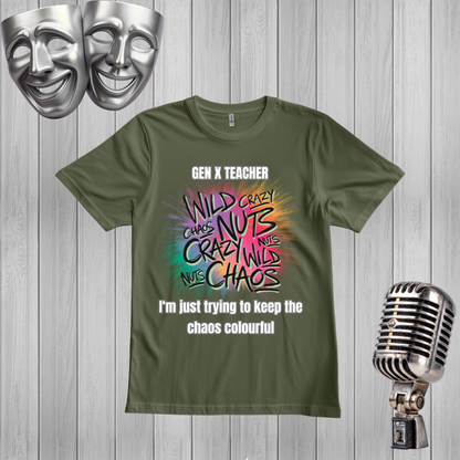 A green graphic t-shirt displayed on a light gray wood plank background, styled with two silver comedy masks in the top-left corner and a vintage silver microphone on the right. The t-shirt features a colorful retro-style graphic with the text 'GEN X TEACHER' and 'I'm just trying to keep the chaos colourful'.