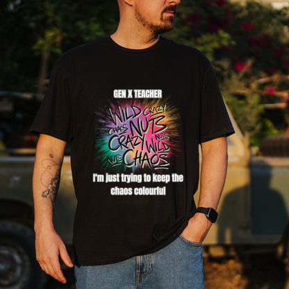 A man wearing a black graphic t-shirt with a colorful 'Gen X Teacher im just trying to keeP the chaos colourful ' design, standing outdoors in front of a blurred vehicle and foliage.