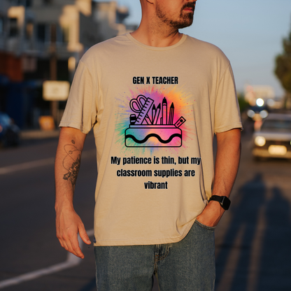 A man wearing a sand graphic t-shirt with a colorful design and text that reads 'GEN X TEACHER My patience is thin, but my classroom supplies are vibrant', standing on a blurred street at sunset.