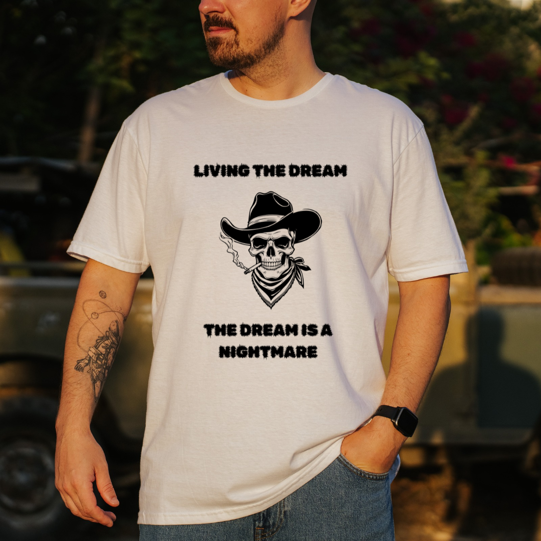 A man wearing a white graphic t-shirt with a black skull wearing a cowboy hat and bandana, with the text 'LIVING THE DREAM THE DREAM IS A NIGHTMARE'.