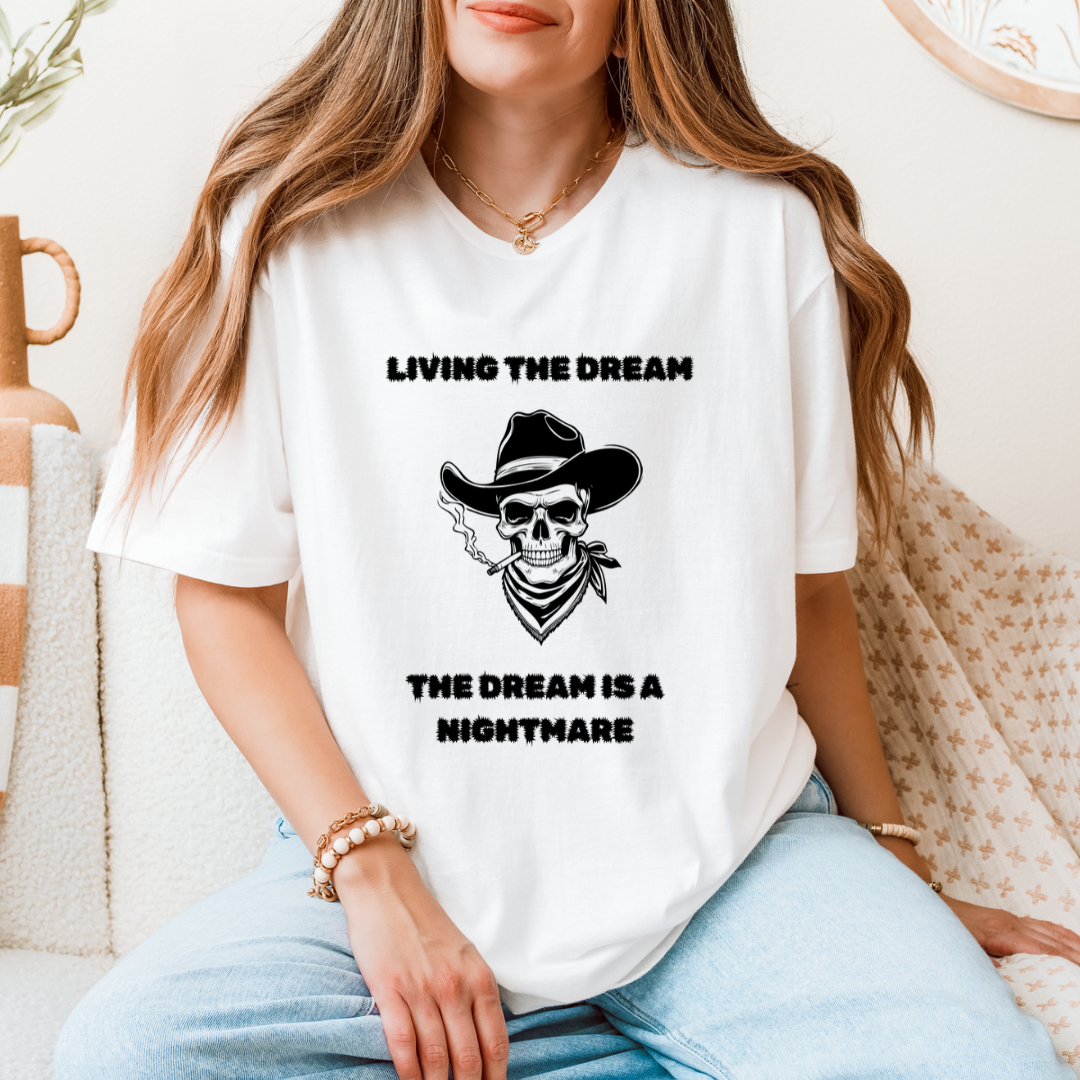 A woman wearing a white graphic t-shirt with a black western skull design and the text 'LIVING THE DREAM THE DREAM IS A NIGHTMARE'.