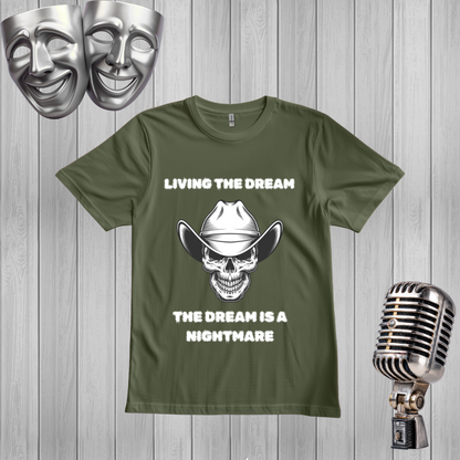 A green graphic t-shirt displayed on a light gray wood plank background, styled with silver comedy and tragedy masks in the top left and a vintage silver microphone in the bottom right. The t-shirt features a white graphic of a skull wearing a cowboy hat with the text 'LIVING THE DREAM' above and 'THE DREAM IS A NIGHTMARE' below.
