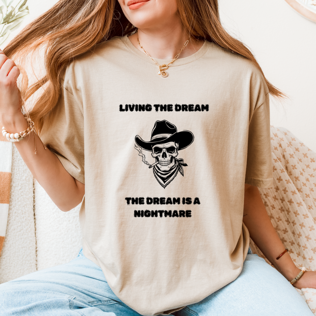 A woman wearing a sand oversized graphic t-shirt with a black skull in a cowboy hat and the text 'LIVING THE DREAM THE DREAM IS A NIGHTMARE'.