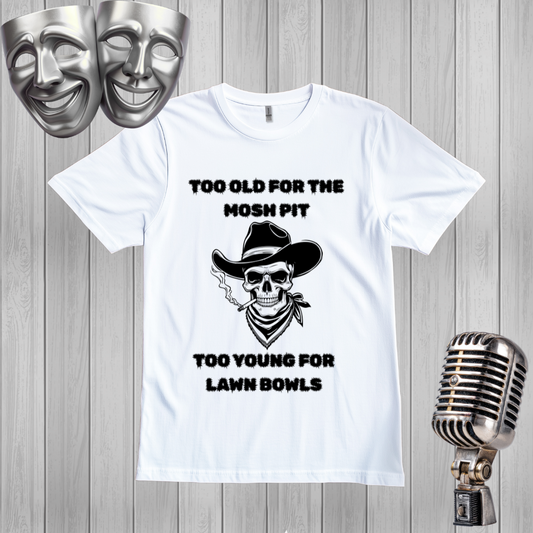 A white graphic t-shirt displayed on a gray wood plank background, flanked by silver comedy and tragedy masks on the left and a vintage silver microphone on the right. The t-shirt features a black graphic of a skull wearing a cowboy hat and bandana, with the text 'TOO OLD FOR THE MOSH PIT' above and 'TOO YOUNG FOR LAWN BOWLS' below.