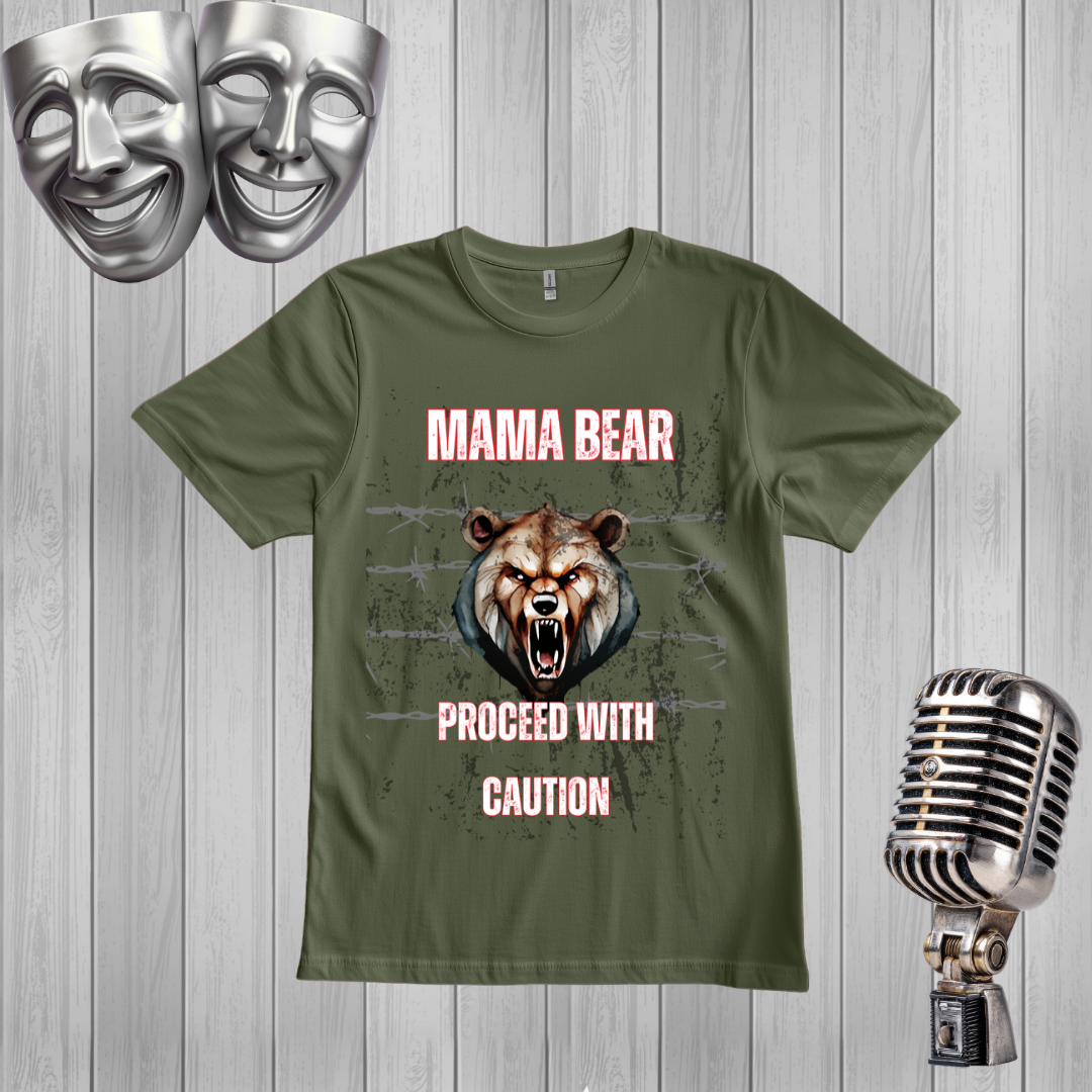 A green graphic t-shirt featuring a roaring bear illustration and the text 'MAMA BEAR PROCEED WITH CAUTION' in pink. The shirt is displayed on a gray wood-plank background with silver comedy and tragedy masks in the top-left corner and a vintage silver microphone on the right.