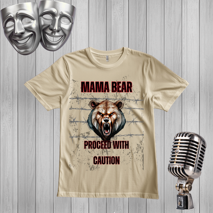 A sand graphic t-shirt featuring a roaring bear design with the text 'MAMA BEAR PROCEED WITH CAUTION'. The t-shirt is displayed on a gray wood-plank background, styled with a silver microphone on the right and two silver comedy and tragedy masks on the top left.