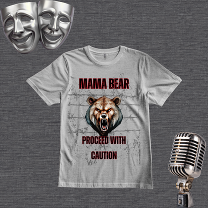 A gray graphic t-shirt featuring a roaring bear design with the text 'MAMA BEAR PROCEED WITH CAUTION' in red and black. The t-shirt is displayed on a textured gray background alongside thematic props, including two silver comedy masks in the top-left and a vintage silver microphone in the bottom-right.