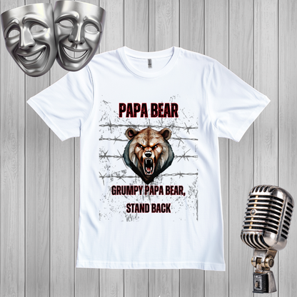 A white graphic t-shirt featuring a grumpy bear design with the text 'PAPA BEAR' and 'GRUMPY PAPA BEAR, STAND BACK'. The shirt is displayed on a gray wood panel background with silver comedy masks in the top-left corner and a vintage silver microphone on the bottom-right.