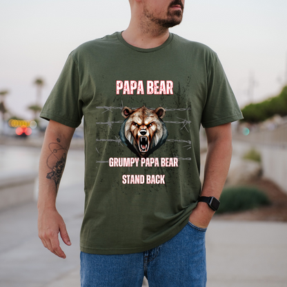 A man wearing a green graphic t-shirt with a grumpy bear design and the text 'PAPA BEAR GRUMPY PAPA BEAR STAND BACK', paired with blue jeans in an outdoor setting.