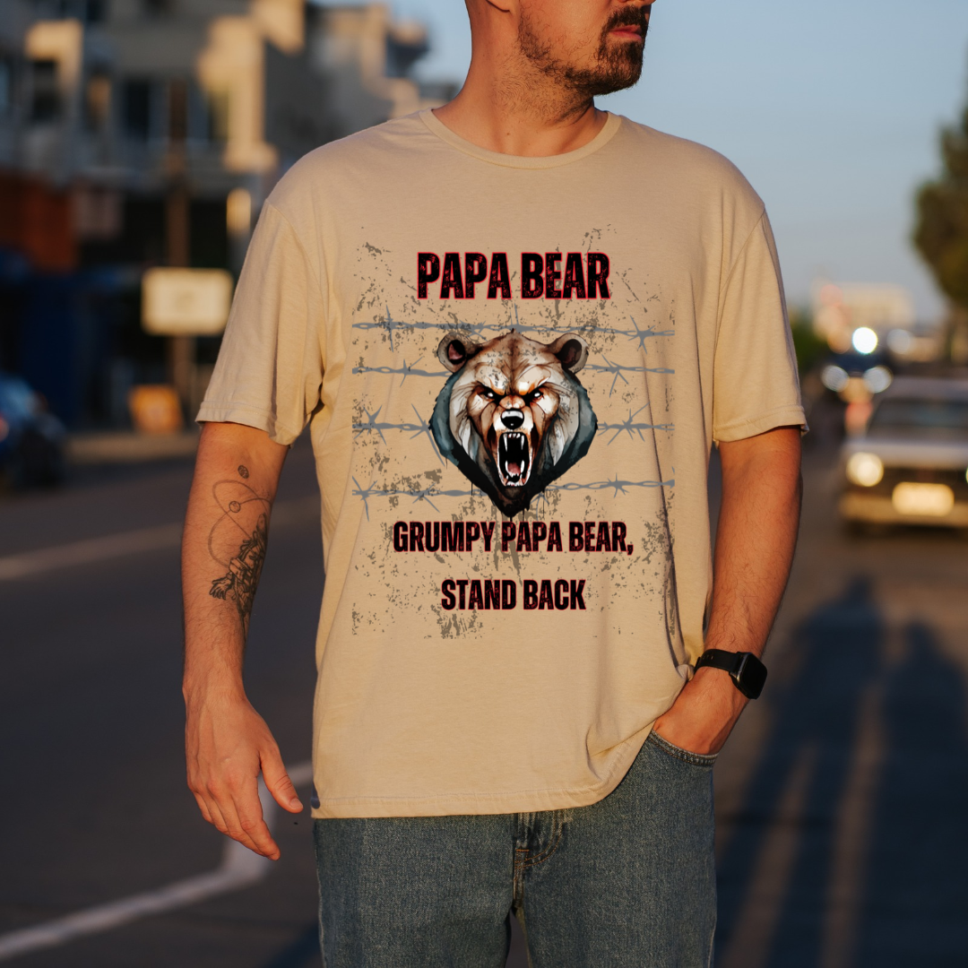 A man wearing a sand graphic t-shirt with a grumpy bear design and the text 'PAPA BEAR GRUMPY PAPA BEAR STAND BACK', standing on a blurred street at sunset.