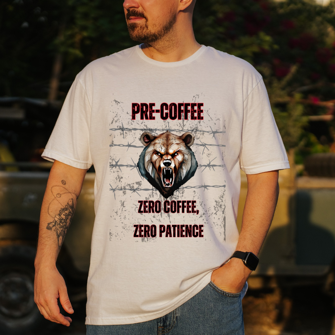 A man wearing a white graphic t-shirt with a grizzly bear design and the text 'PRE-COFFEE ZERO COFFEE, ZERO PATIENCE' in red and black, set against an outdoor background.
