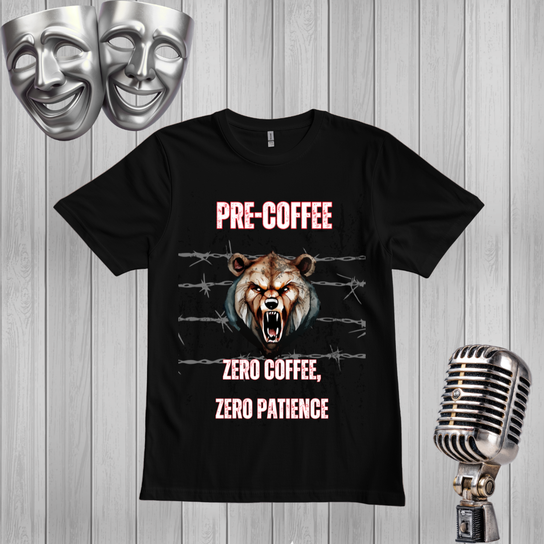 A black graphic t-shirt displayed on a light gray wood plank background, flanked by two silver comedy masks on the top left and a vintage silver microphone on the bottom right. The t-shirt features a graphic of a snarling bear with glowing orange eyes, barbed wire, and the text 'PRE-COFFEE' and 'ZERO COFFEE, ZERO PATIENCE' in pink and white.