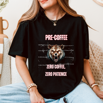 A woman wearing a black graphic t-shirt with a roaring bear design and the text 'PRE-COFFEE ZERO COFFEE, ZERO PATIENCE' in pink, sitting on a beige couch.